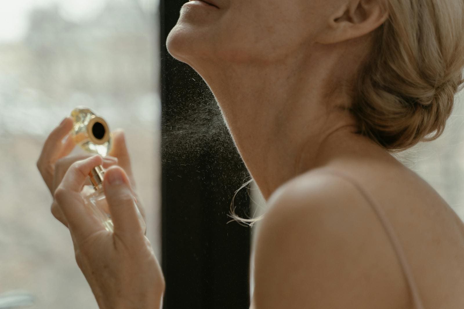 Close-up of a woman applying perfume with a glass bottle in natural light.